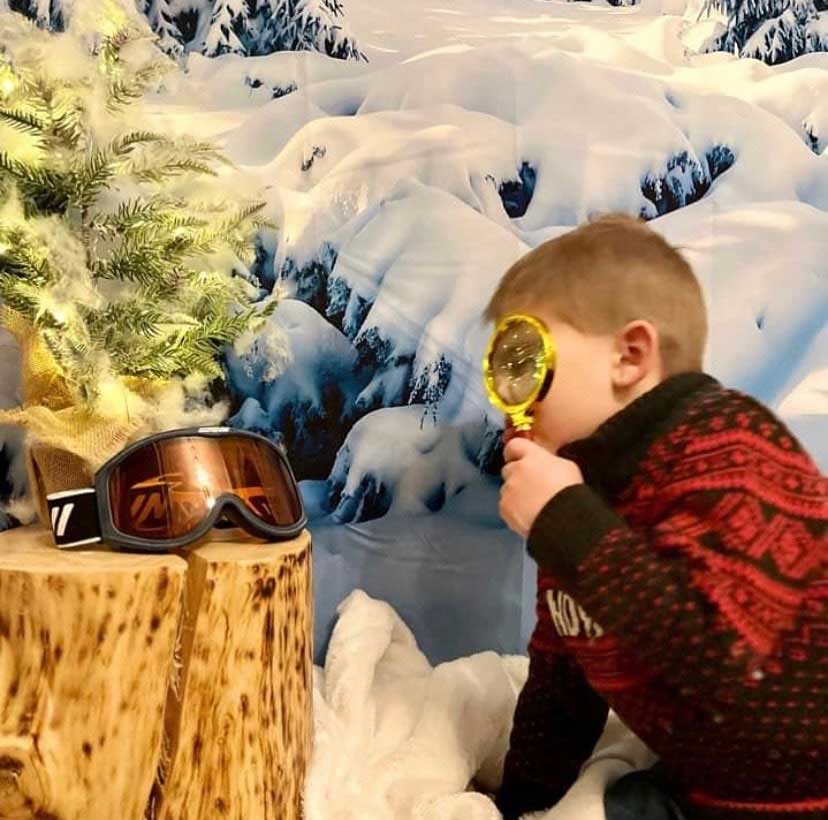 Child looks at ski mask through a magnifying glass at a Murder in the Alps Mystery Party